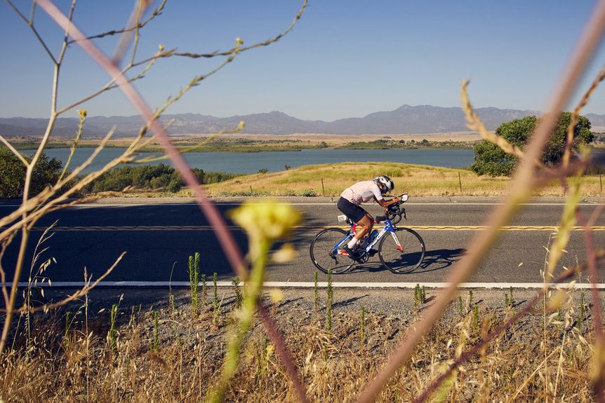 Dorina riding a Californian road beside a lake, mountains behind her
